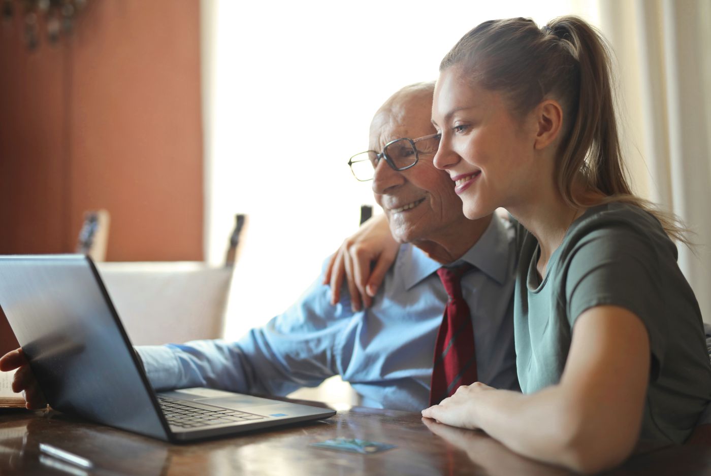A younger woman helping an older man feel confident using a laptop